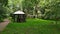 Gravel path in green summer forest leading to a wooden gazebo for making grill