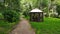 Gravel path in green summer forest leading to a wooden gazebo for making grill