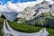 Gravel road turn in the Swiss Alps, around Grindenwald, with rocky peaks shrouded in clouds in the background, and green pastures