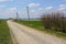 Gravel rural road along a green field against a blue sky