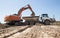Gray articulated dump truck and crawler excavator at a construction site during loading of soi
