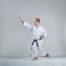 On a gray background, an adult sportsman trains a formal karate exercise