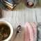 on a gray background, flower tea is next to the knitting, and next to the books is an aroma candle on which mittens lie