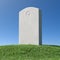 Gray blank gravestone on green grass hill under blue sky