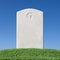 Gray blank gravestone on green grass under blue sky close-up