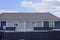 Gray blue private house with windows under a  tiled roof behind a metal fence