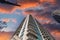 A gray and blue skyscraper with metal balconies near an office buildings with powerful clouds at sunset