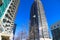 A gray and blue skyscraper and office buildings with metal balconies with tall black light posts and bare winter trees