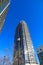 A gray and blue skyscraper and office buildings with metal balconies with tall black light posts and bare winter trees