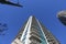 A gray and blue skyscraper and office buildings with metal balconies with tall black light posts and bare winter trees