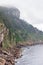 Gray calm waters of Cantabrian sea meet sheer cliffs of Cabo Antzoriz promontory covered with emerald moss on hazy summer morning