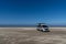 Gray camper van parked on an endless white sand beach in the middle of nowhere with ocean behind