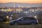 Gray car parked at night in green meadows on background of lights of distant city buildings and dark mountain ridge under bright