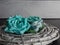 Gray coiled wood bound together on a black slate and gray background with teal paper flower rose blooms