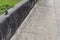 Gray concrete retaining wall along a driveway with grass and weeds