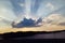 Gray cumulus on a blue sky covering the sun with sun rays coming out from behind the cloud. A large gray-white cloud with bright