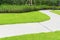 The gray curve pattern walkway in a beautiful garden, sand washed finishing on concrete paving, a smooth green grass lawn, trees