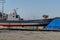 Gray fishing trawler dry docked in gravel lot