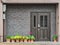 Gray front door with small square decorative windows and flower pots in fron of it