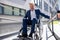 Gray haired businessman in formal wear gets to work in wheelchair rides ramp.