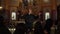 A gray-haired Catholic priest conducts a Sunday service. The priest throws up his hands and looks up while praying.