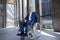 Gray haired disabled man wearing official style suit in wheelchair city background.