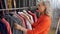 Gray haired elderly woman choosing dress in fashionable clothing store. Elegant woman choosing clothes in new fashion