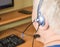 A gray-haired fat old man with a headset looks at the monitor screen, remote work, computer technology for pensioners, adaptation