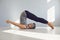 Gray haired flexible man practicing yoga in plow pose in light modern studio