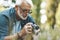 A gray-haired grandfather with a beard photographs flowers in the forest, a hobby in the fresh air. A keen amateur