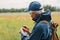 Gray haired man in jacket and cap treasure hunter looking at his finding, holding old coin under ground when searching in meadow