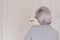 A gray-haired older woman in a gray turtleneck has a cute beige cat on her shoulder. The view from the back