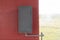 A gray iron box hangs on a red wall, next to a window. Fire box or gas box, a water or gas pipe is connected