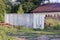 A gray iron container stands in the grass near the house