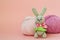 Gray knitted hare stands on the background of multi-colored balls of yarn on a pink background. There is a place for text