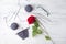 Gray knitting wool, half of handmade sock on needles, black glasses and single red rose on wooden white background.