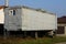 Gray long metal trailer with a window on wheels in the grass on the street