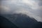 A gray low cloud on a high peak. High black rock in low clouds. Surreal gloomy mountains