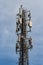 Gray metal cell tower carrying antennas of cellular networks on the blue sky with white clouds background in sunny day. Vertical