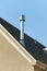 Gray metal chimney pipe on modern roof with shady tiles on bright sunny beige stucco painted house in midday sun