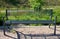 Gray metal park bench with transparent design of metal wires cross bars path in the park flowerbed in the background beige gravel