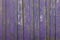 Gray old fence a wall of wooden planks with purple peeling paint and cracks and white spots. vertical lines. rough surface texture