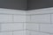 Gray painted wall, part of the wall is covered tiles small white glossy brick, ceramic decorative molding tiles, detail of intrica
