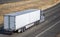 Gray powerful industrial big rig semi truck transporting cargo in dry van semi trailer running on the summer divided highway road
