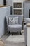 Gray small cozy armchair in the interior with a soft pillow. Corner for relaxation and reading in the interior