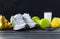 Gray sneakers, green dumbbell, bananas, lemon, Apple, sports bracelet, glass of milk on a dark background