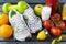 Gray sneakers, green dumbbell, glass of milk, tomatoes, oranges, Apple, lemon, sports bracelet, tape on a gray background