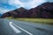 Gray two-lane road with stripes and arrow on the background of mountains. Asphalt pavement of a two-lane highway