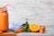 A gray wooden table with a board, mason jar full of carrot smoothie with basil, orange and mint on a blurred background.