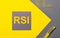 On a gray and yellow background, a gray sticker with yellow text RSI Relative Strength Index, yellow paper clips and a yellow pen